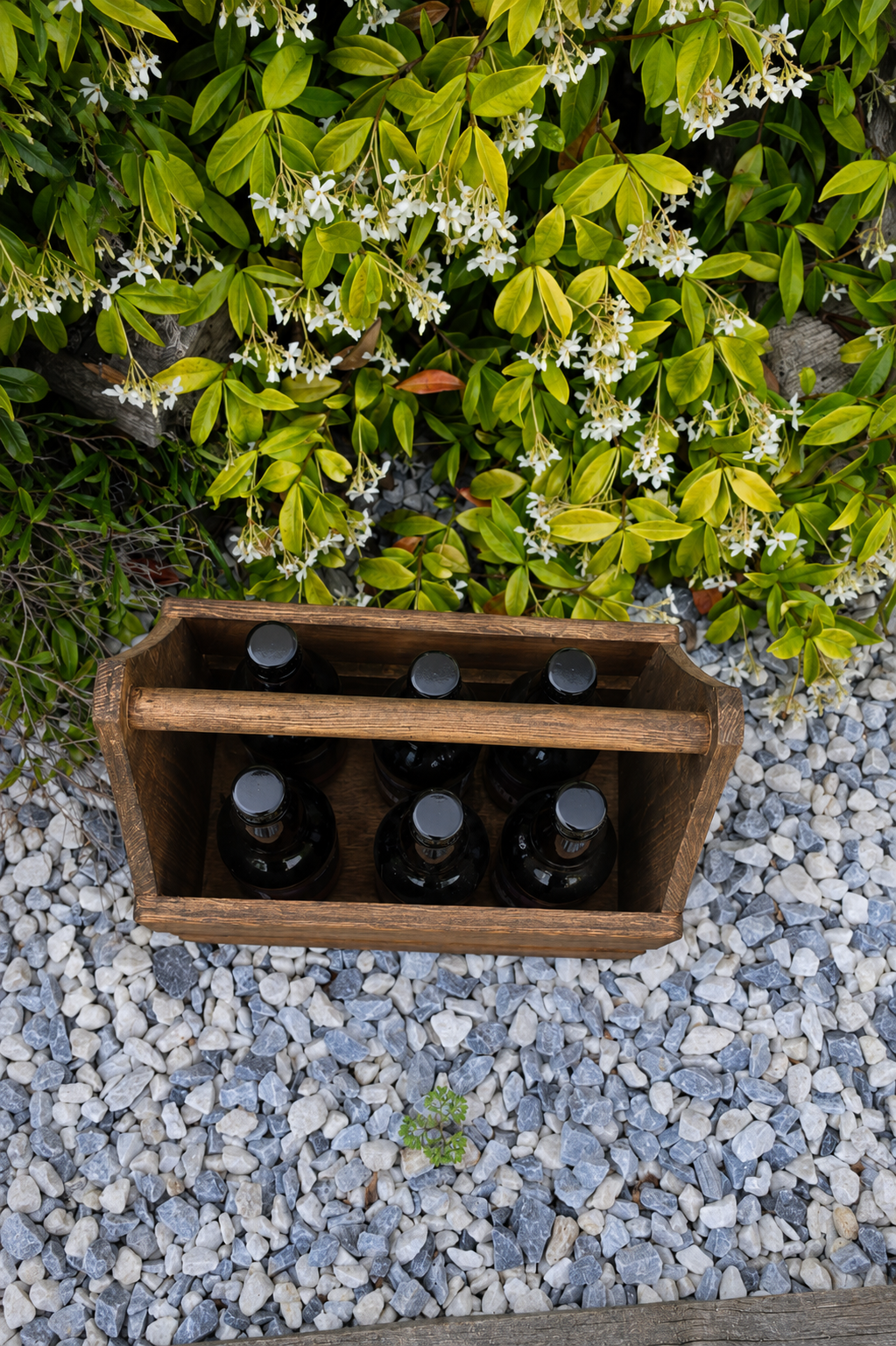 Wooden crate with bottles on a pebble surface with greenery in the background